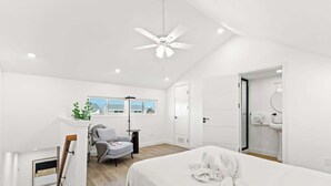 A modern bedroom with a large bed, a ceiling fan, a desk, and a chair.