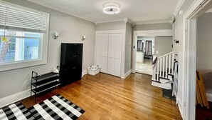 Une pièce spacieuse avec un plancher en bois, un tapis rayé noir et blanc, un meuble noir, un panier à linge blanc et une armoire blanche.