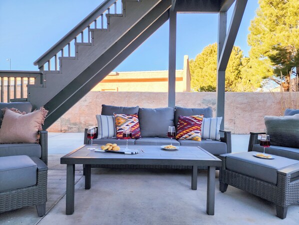Un patio exterior con un conjunto de sofás, una mesa con vasos y aperitivos, y una escalera.