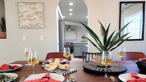 A dining area with a wooden table set for a meal, a large plant centerpiece, and a view into the kitchen.