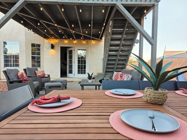 An outdoor patio with a wooden deck, seating area, and a staircase leading to an upper level.
