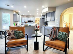 Una cocina moderna con armarios grises, una isla central y un comedor con dos sillas de cuero y una mesa redonda pequeña.