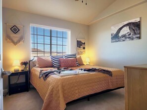 A bedroom with a bed, bedside tables, a window, and a painting on the wall.