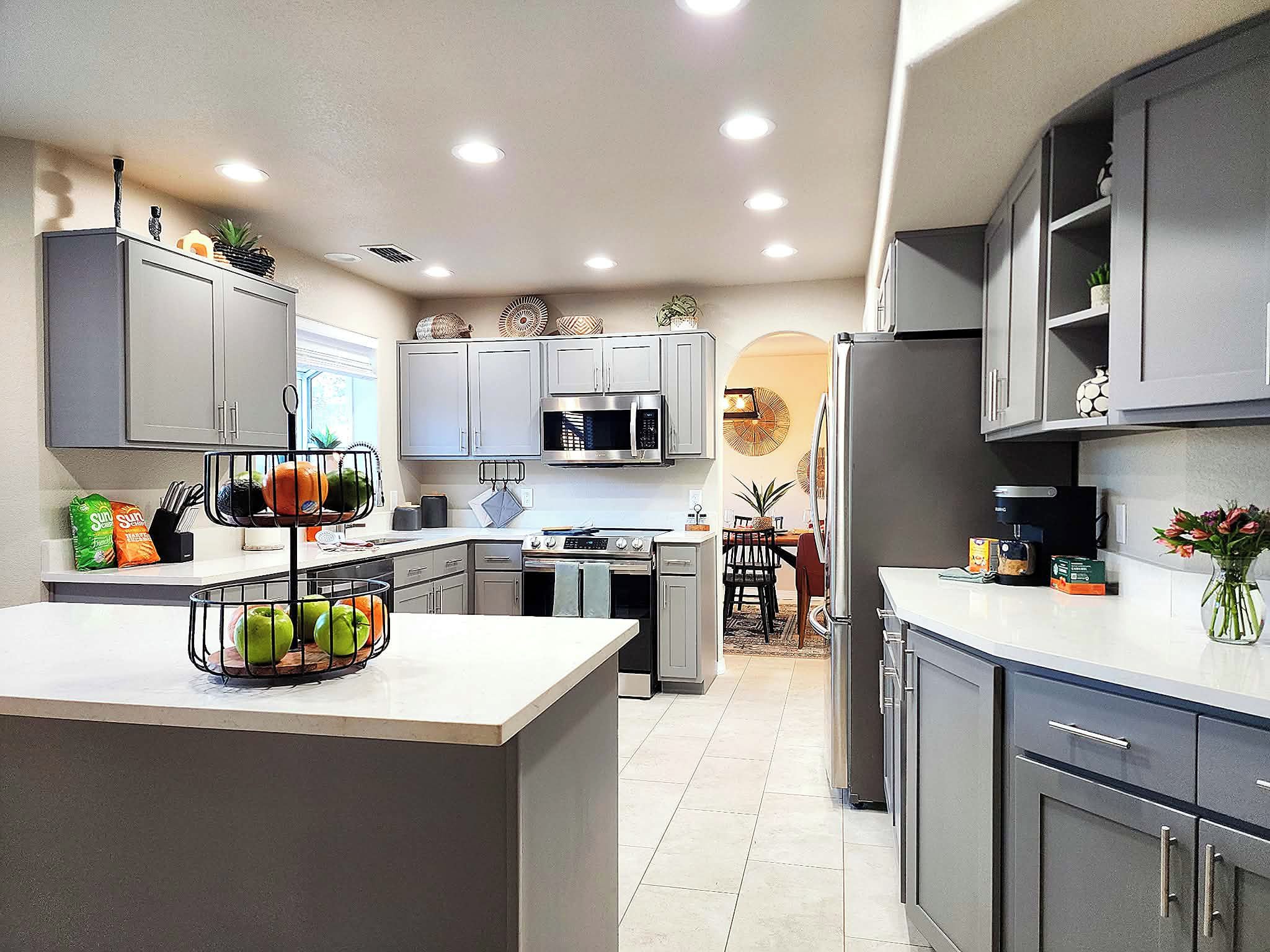 A modern kitchen with grey cabinets, a built-in microwave, and a central island with a fruit basket.