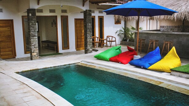 Una piscina con coloridos puffs y un paraguas azul.