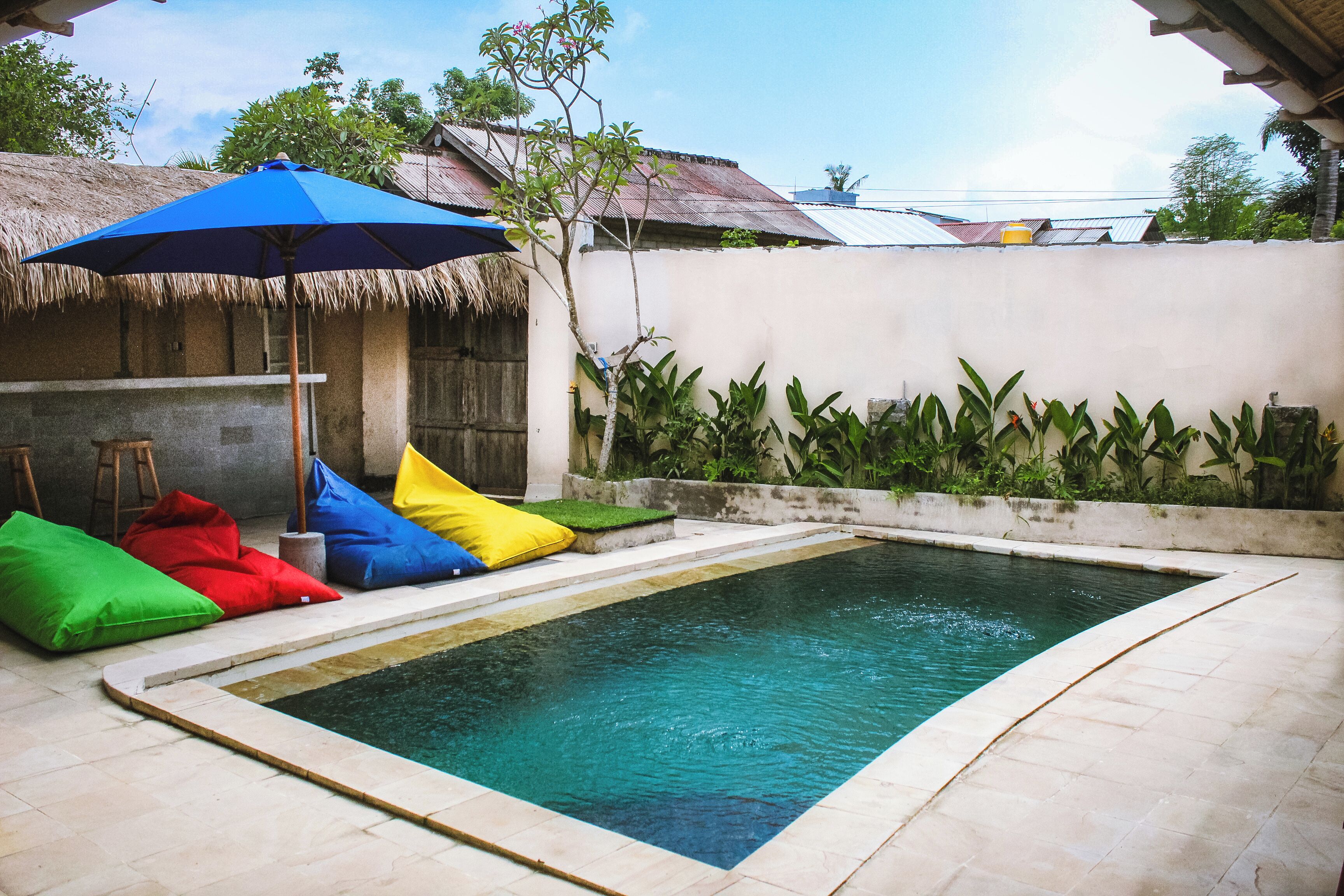 Piscina con cojines de colores y una sombrilla azul.