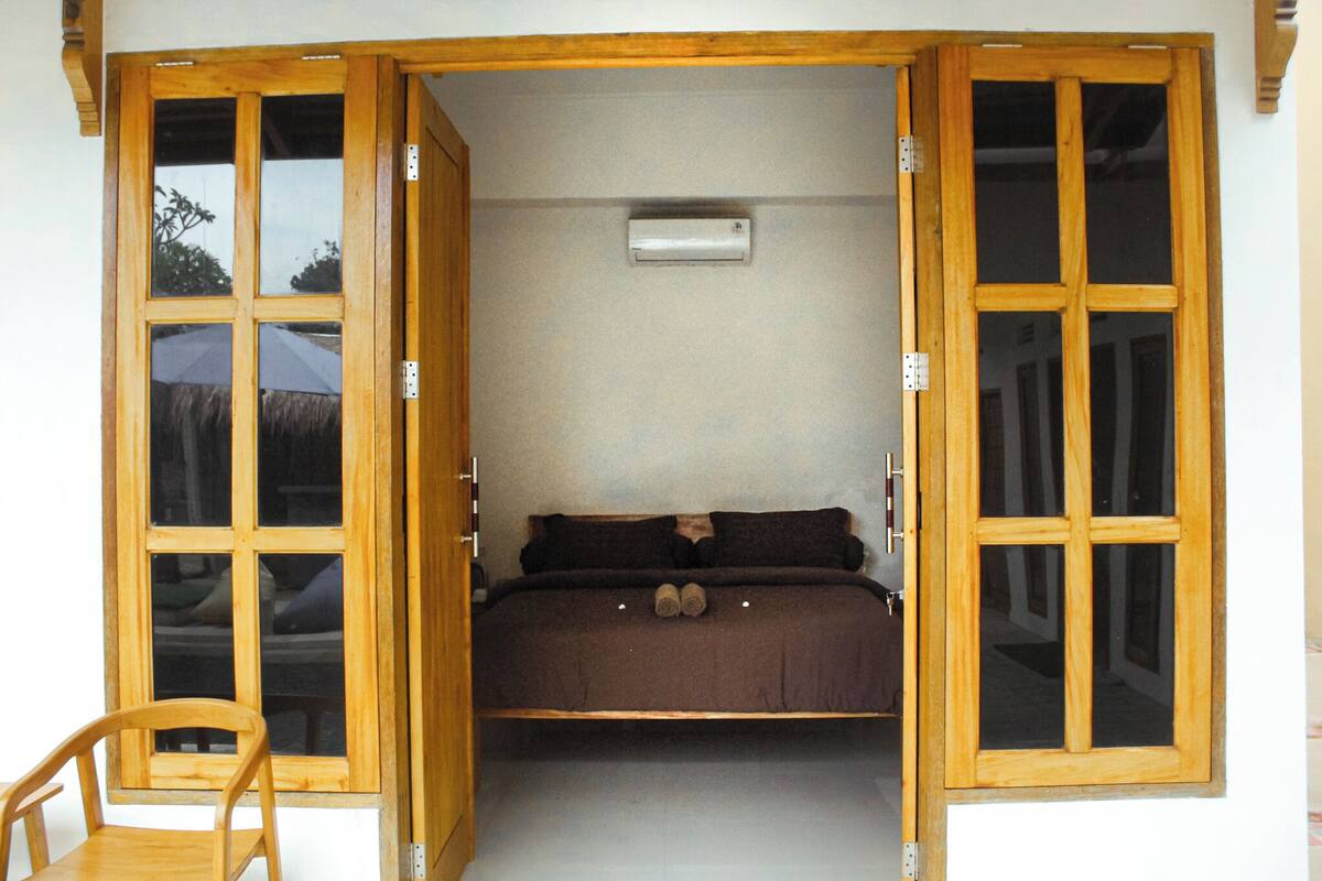 A room with a bed, a chair, and a window with a view of a car and trees.