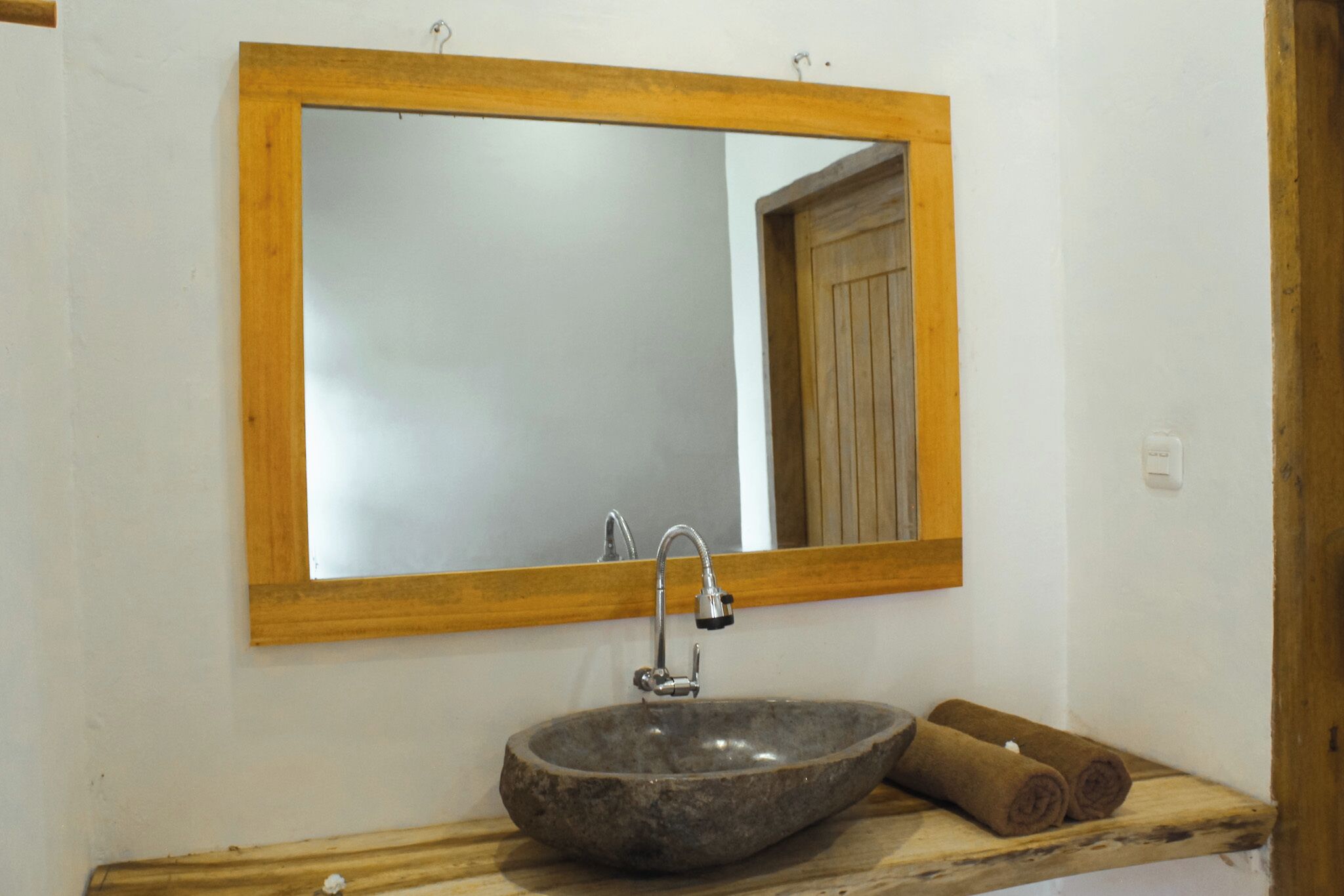 Un baño con un espejo de marco de madera, un lavabo de piedra y un estante de madera con toallas.