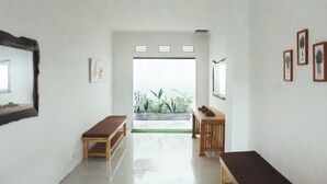 Un pasillo con un banco, una mesita y una puerta que da a un balcón con plantas.