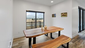 A modern interior with a wooden dining table and bench, a large window with a view of mountains, and two framed pictures on the wall. - Stunning Penthouse Breathtaking Water Views! 302 (Juneau)