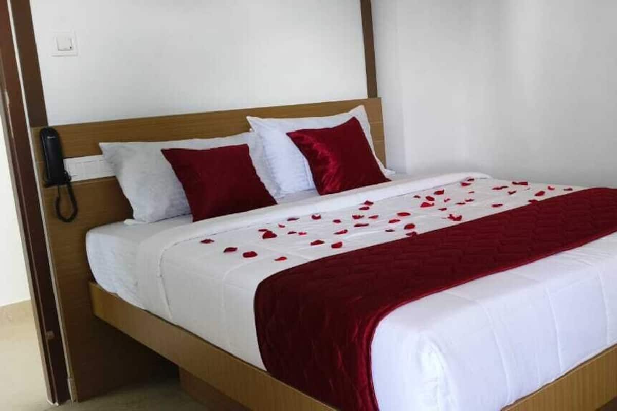 A neatly made bed with white and red bedding, a wooden headboard, and a bedside phone.