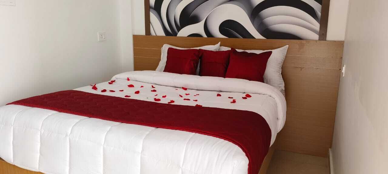 A neatly made bed with a white and red bedspread, a wooden headboard, and a wall with a large abstract painting.