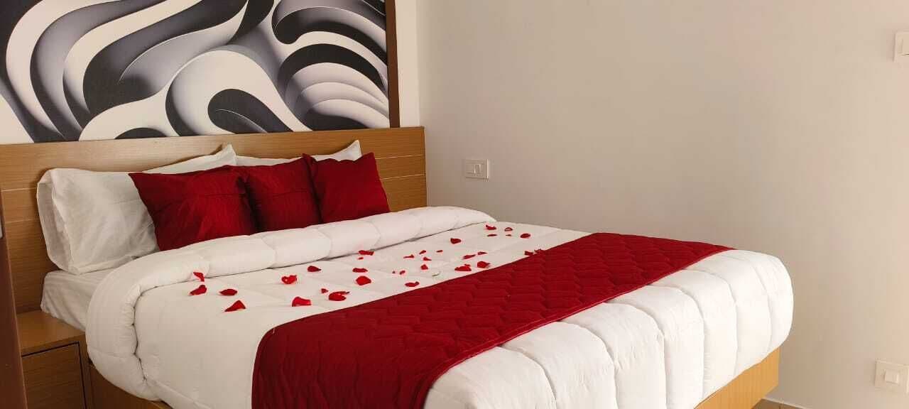 Una cama bien hecha con ropa de cama roja y blanca, un cabecero de madera y una pared con un diseño abstracto moderno.