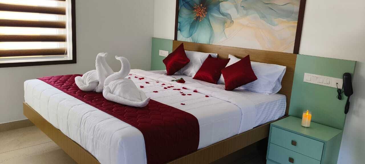 A neatly made bed with a red blanket, two white towels arranged as swans, and red pillows. There is a nightstand with a phone and a candle.
