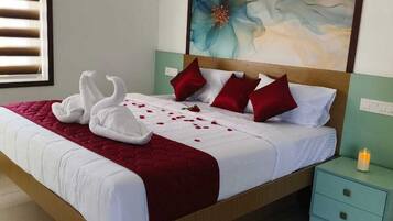 A neatly made bed with a red blanket, two white towels arranged as swans, and red pillows. There is a nightstand with a phone and a candle.