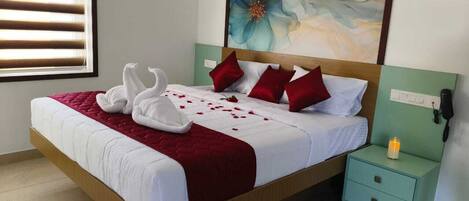A neatly made bed with a red blanket, two white towels arranged as swans, and red pillows. There is a nightstand with a phone and a candle.