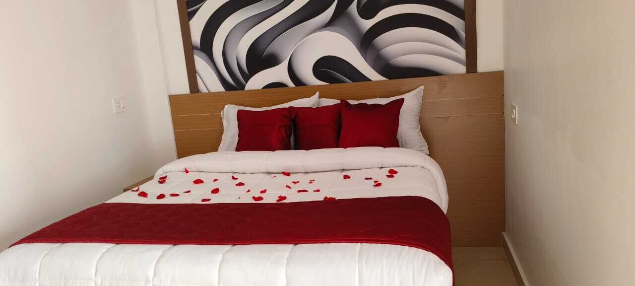 A neatly made bed with red and white bedding, a wooden headboard, and a wall with a black and white abstract design.