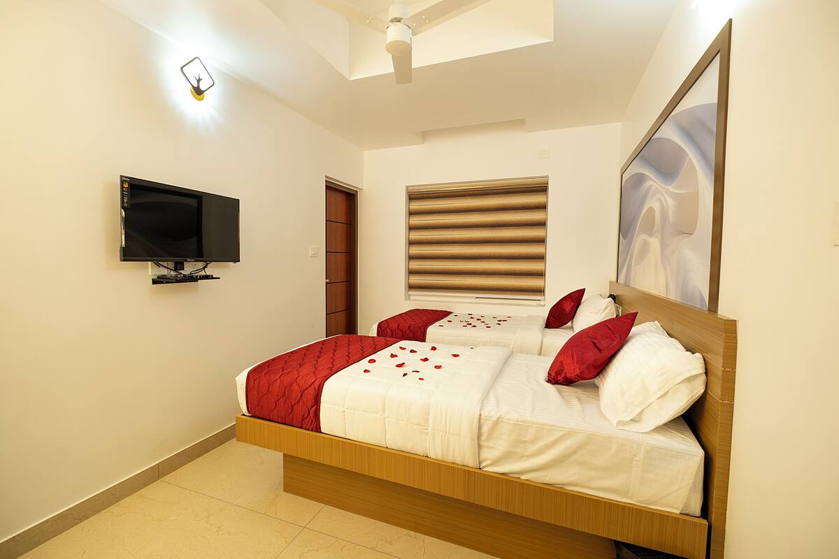 A bedroom with a bed, a television mounted on the wall, a window with blinds, and a ceiling fan.