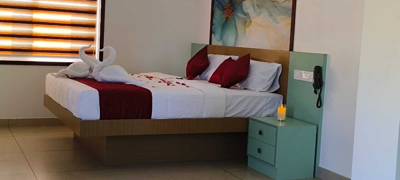 A neatly made bed with a red and white bedspread, a pair of red pillows, and a decorative swan. There is a bedside table with a phone and a candle.