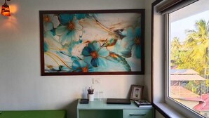 Ett rum med en stor blomstermålning på väggen, ett skrivbord med en bärbar dator, en inramad bild och ett fönster med utsikt över palmer.
