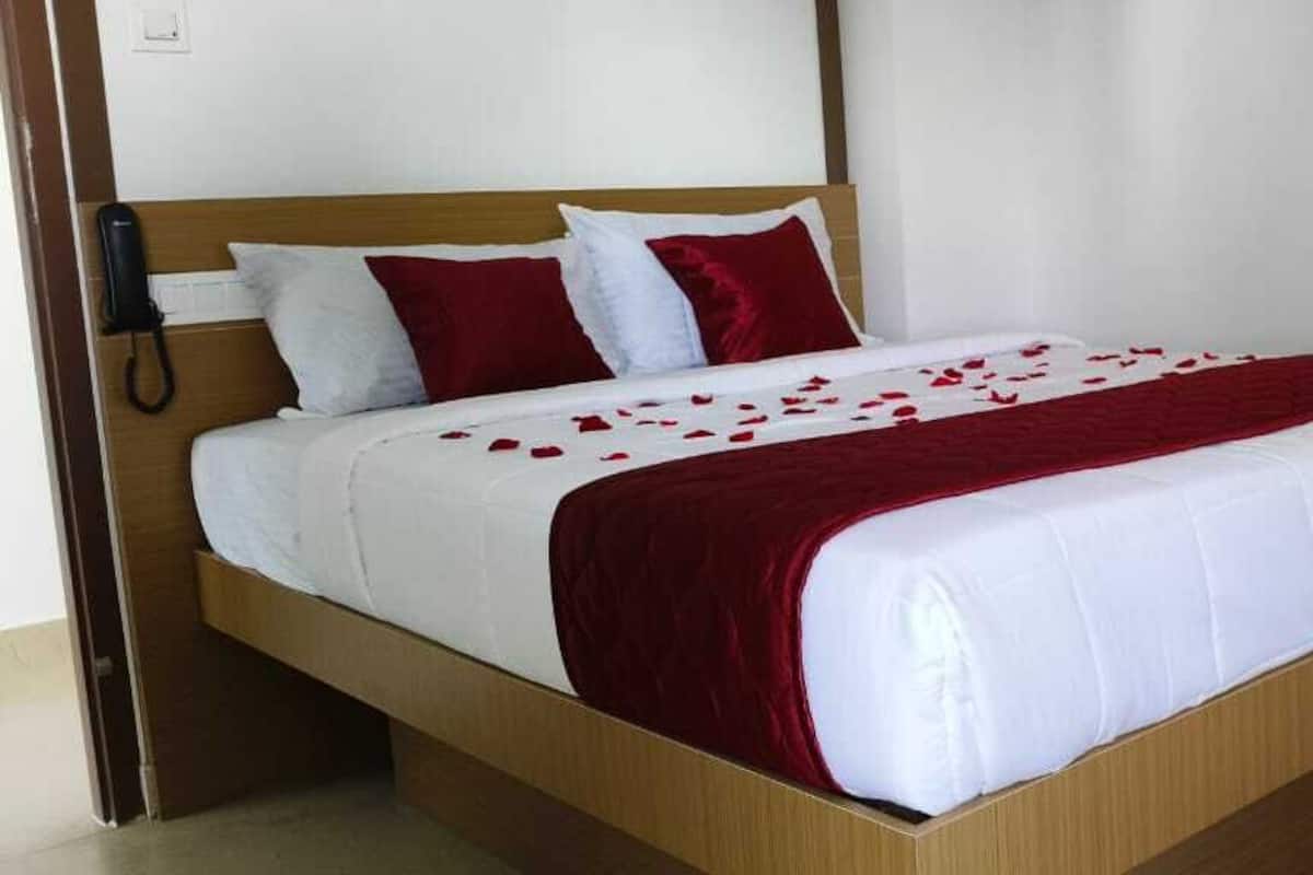 A bed with white and red bedding, a wooden headboard, and a telephone on the side.