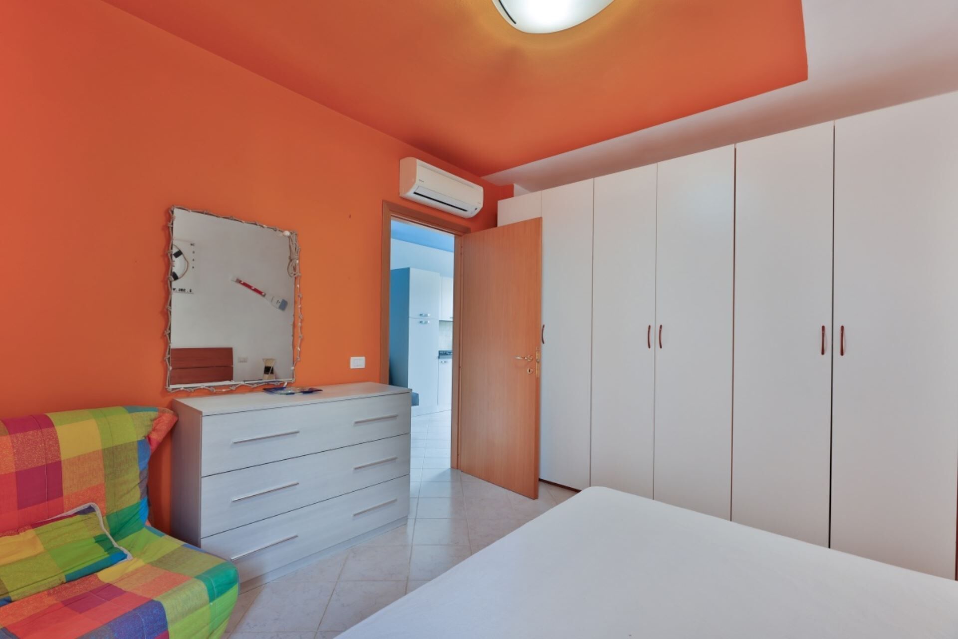 A bedroom with a colorful bed, a white dresser, and a wardrobe.