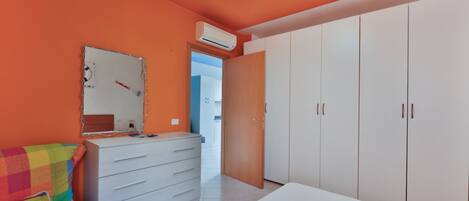 A bedroom with a colorful bed, a white dresser, and a wardrobe.