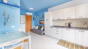 Una cocina compacta con armarios blancos, una mesa de comedor con sillas y una pared azul decorada.