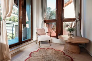 A room with a large window, a chair, a round table, and a rug.