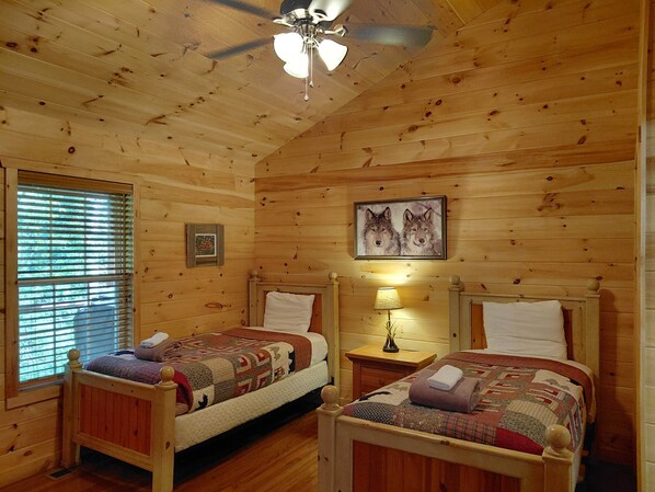 Un dormitorio tipo cabaña con dos camas de madera, un ventilador de techo y una ventana con persianas.