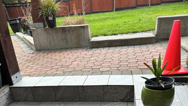 A set of stone steps leading to a patio area with potted plants and a red cone.
