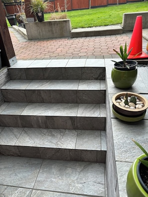 Un conjunto de escalones de piedra que conducen a un patio con plantas en macetas y un cono rojo.