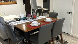 A dining area with a wooden table, grey chairs, and a black and white patterned table runner. There is a painting of a cityscape on the wall, and a sign that reads "LONDON" above the door.