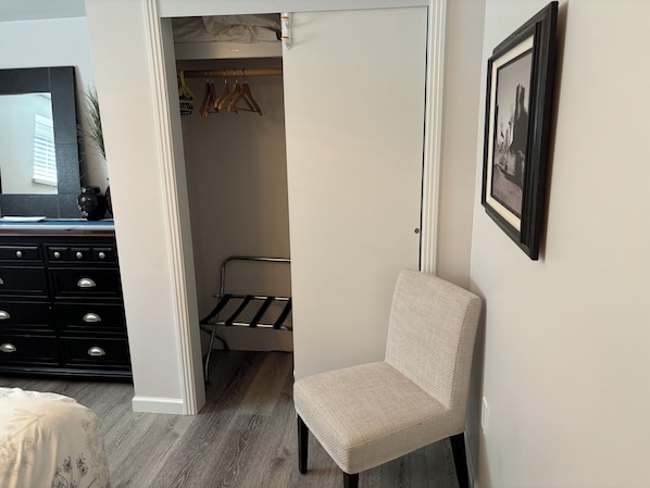 Un dormitorio con cama, una silla, un armario y un cuadro en la pared.