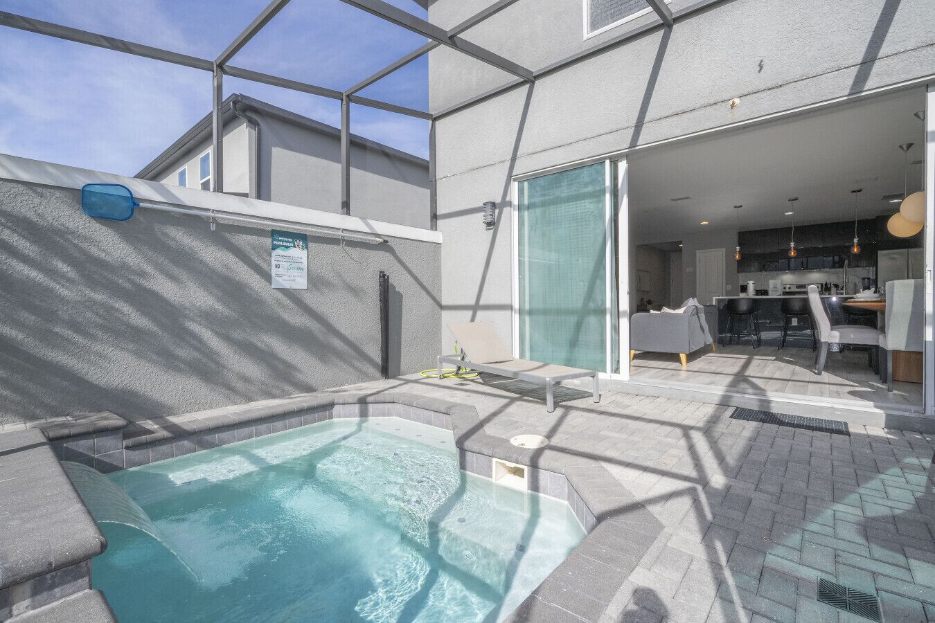 Un espace piscine extérieur moderne doté d’un jacuzzi, d’un coin salon et offrant une vue sur la cuisine et la salle à manger adjacentes.