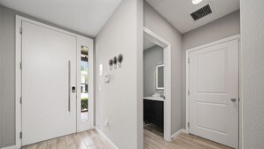 Un couloir avec deux portes blanches, un interrupteur et une grille de ventilation au plafond.