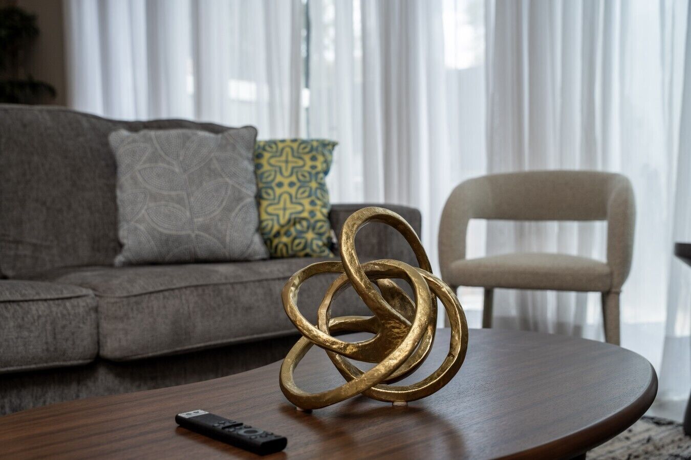 Een woonkamer met een bank, een gestreept kussen, een decoratieve metalen sculptuur, een afstandsbediening en een fauteuil.