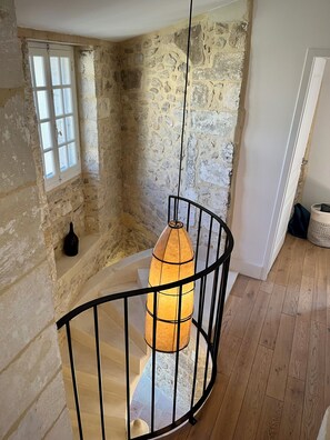 Un escalier en colimaçon avec un luminaire suspendu, des murs en pierre et un plancher en bois.