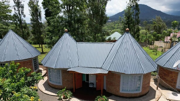 A cluster of small, circular buildings with conical roofs, surrounded by greenery and a mountainous backdrop.