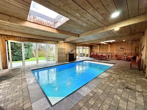 An indoor swimming pool with a clear view of the outside, wooden walls, and a patio area with outdoor furniture. - Gite all-in with an indoor pool, sauna and games (Sourbrodt)