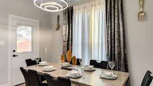 Une salle à manger avec une table rectangulaire dressée pour quatre personnes, des chaises noires et un luminaire suspendu moderne.
