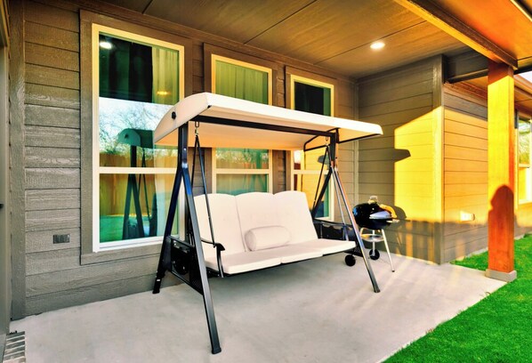 A porch with a swing chair, a small table, and a chair.
