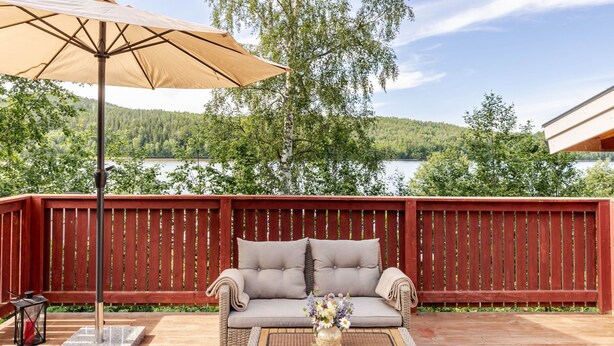 A deck with a red fence, a beige sofa, and a table with a vase of flowers. - Sjödrömmen by Interhome (Hudiksvall)