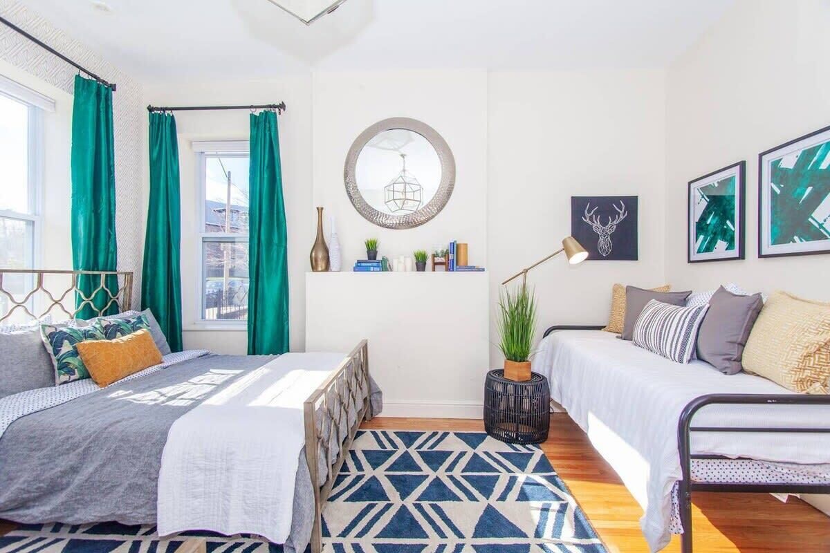 A modern bedroom with two beds, a geometric patterned rug, a round mirror, and artwork on the walls.