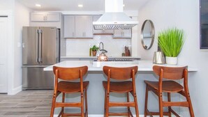 Una cocina moderna con un refrigerador de acero inoxidable, una estufa a gas y taburetes de bar de madera.