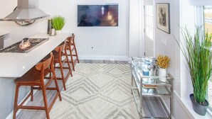 Una cocina moderna con una isla central, taburetes de bar, una campana extractora de acero inoxidable y un televisor de pantalla plana montado en la pared.