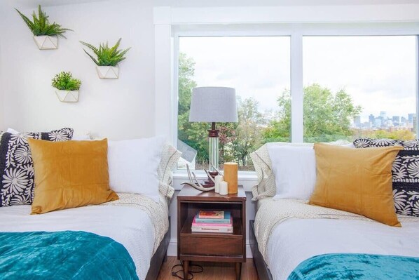 A bedroom with two beds, a nightstand with books and a lamp, and three potted plants on the wall. - Cozy Duplex | Near T (Boston)
