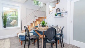 Un comedor con una mesa redonda, sillas negras y una escalera al fondo.