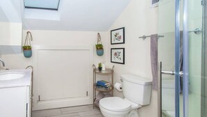 Een moderne badkamer met dakraam, toilet, wastafel en douchehoek.