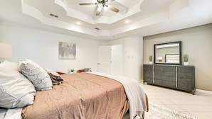 A bedroom with a bed, ceiling fan, and a large mirror above a dark-colored dresser. - Fenced Yard: Home Near Hospitals in Edinburg! (Edinburg)